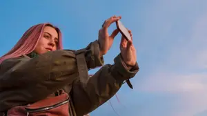 A young woman taking a photo on her phone, representing digital photo hoarding and difficulty deleting images.