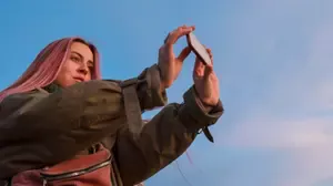 A young woman taking a photo on her phone, representing digital photo hoarding and difficulty deleting images.