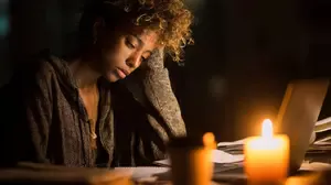 A tired woman working late at night with papers and a laptop, showing signs of work burnout and emotional exhaustion.