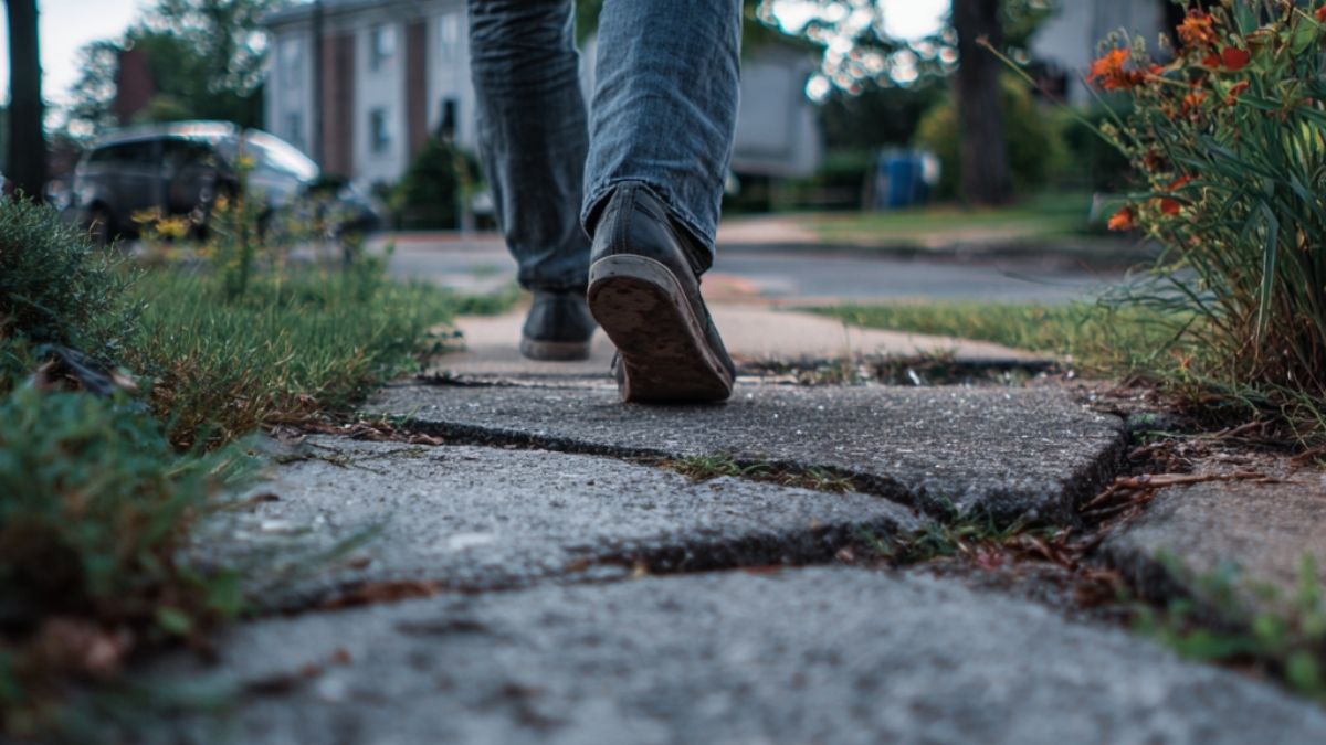 Person walking over a cracked sidewalk with a clear trip hazard, illustrating the risk of injuries on public property.