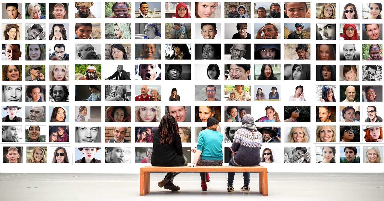 three people sat on a bench looking at a large photo gallery of human faces.