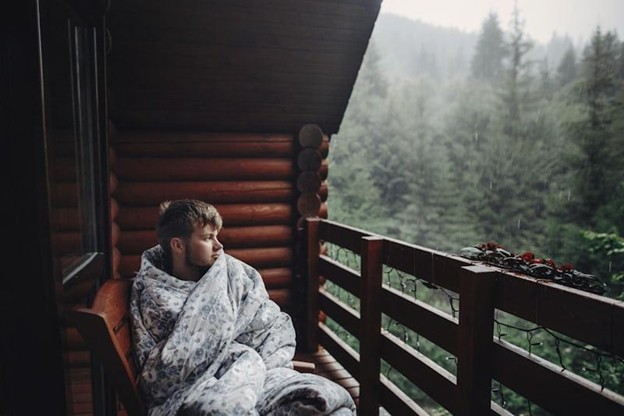 Person wrapped in a blanket looking outside during winter, illustrating isolation and low mood associated with seasonal affective disorder.
