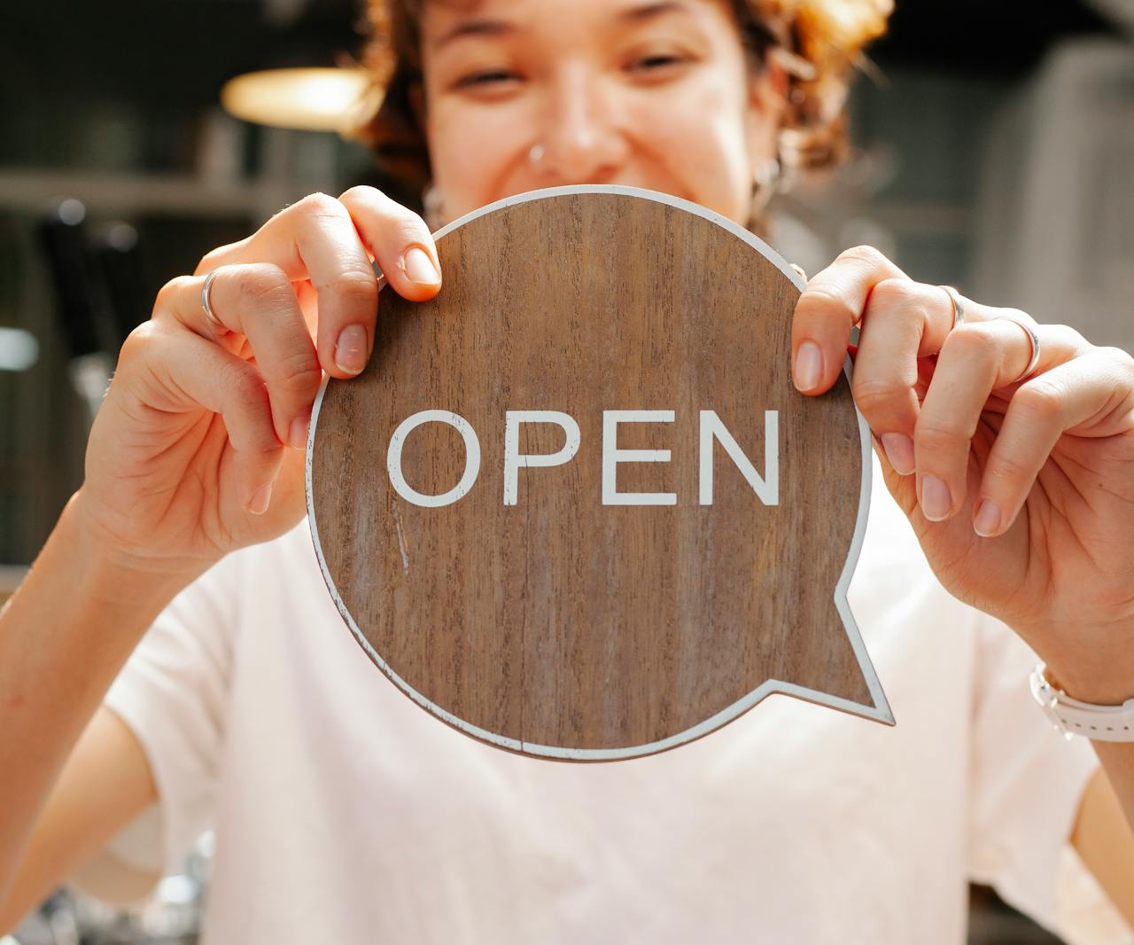Happy woman showing wooden signboard saying open Happy woman showing wooden signboard saying open