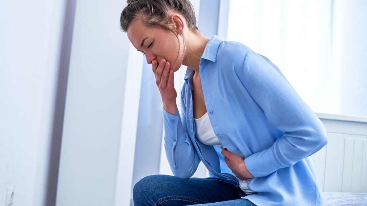 A woman holding her stomach and covering her mouth, showing nausea and abdominal pain after food poisoning. A woman holding her stomach and covering her mouth, showing nausea and abdominal pain after food poisoning.
