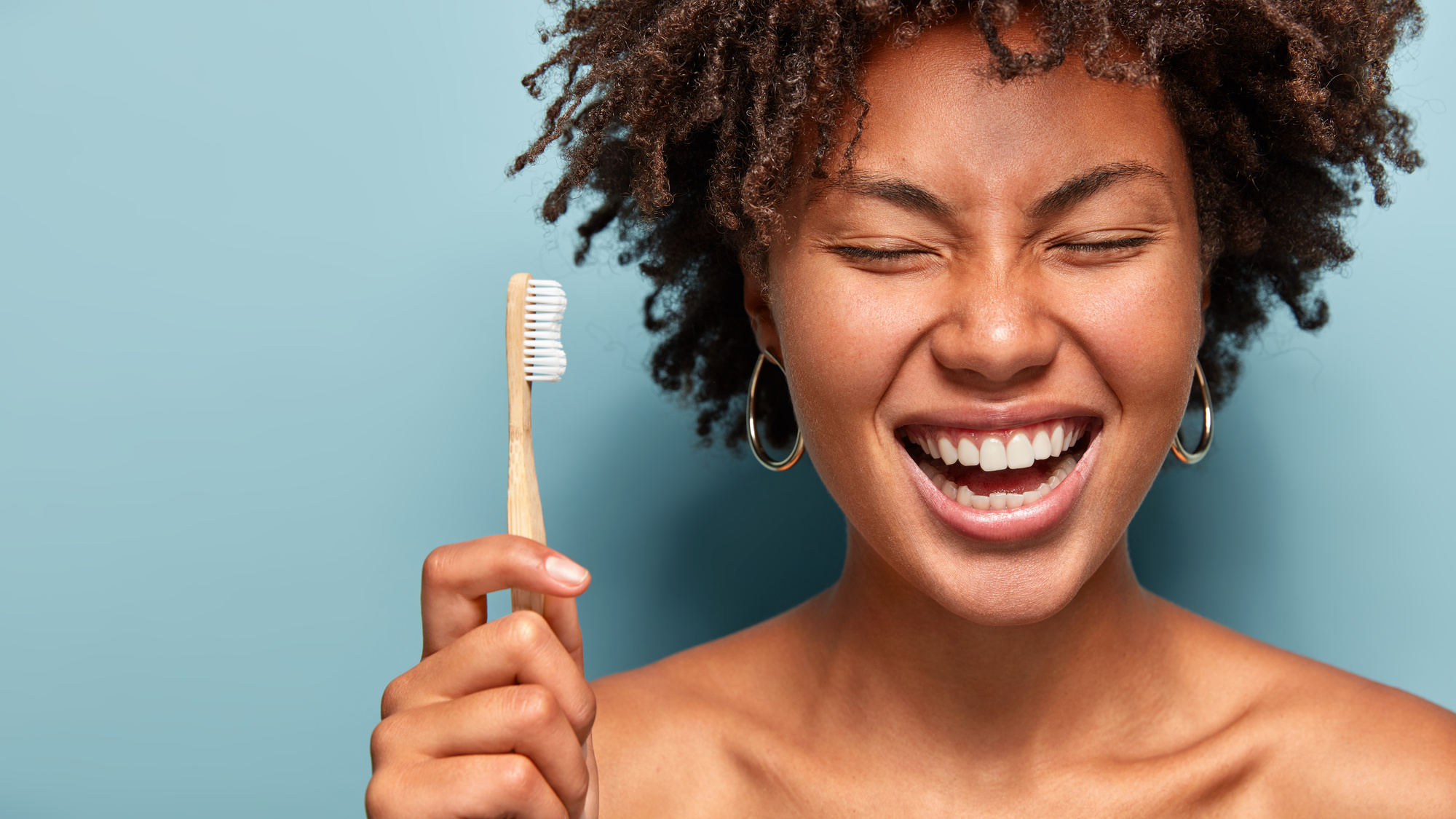 Happy smiling woman with curly hair laughs and shows bright smile while holding toothbrush