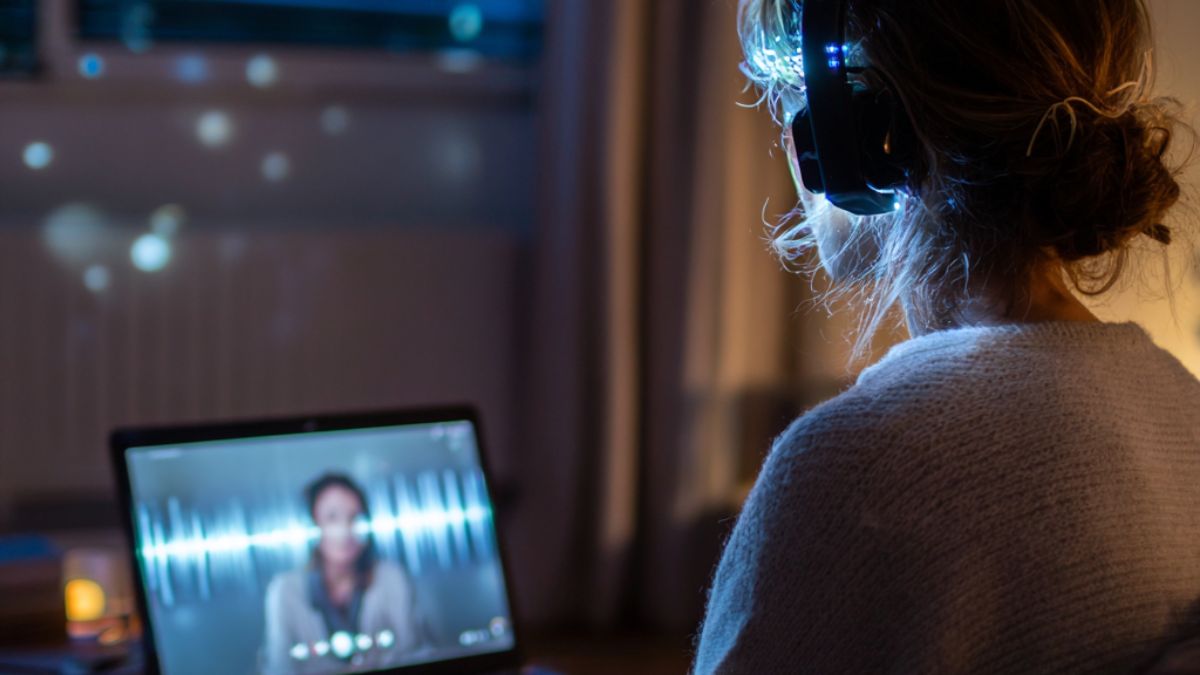 Woman participating in a virtual EMDR therapy session at home, wearing headphones and focusing on a laptop screen with a therapist visible via video call.